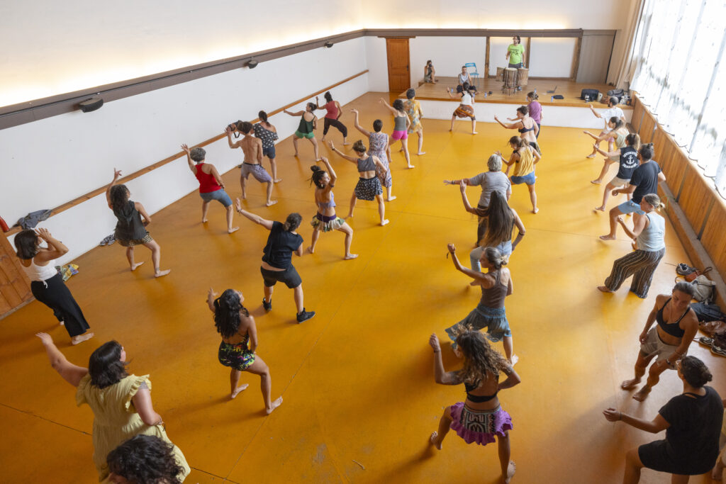Foto de un grupo de participantes durante un taller de danza africana en el auditorio del museo La Casa de las Gentes, las personas de pie realizando movimientos
